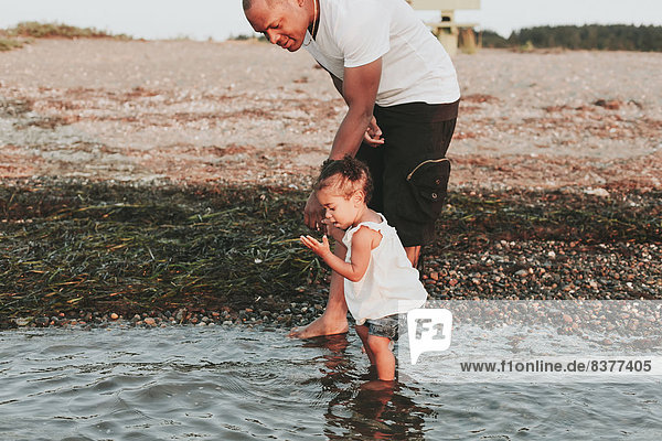 Father Wading In Water With Daughter By Beach  British Columbia  Canada