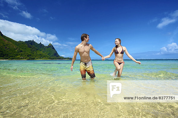 A couple holding hands and walking in the ocean water Wailua  Hawaii  United States of America