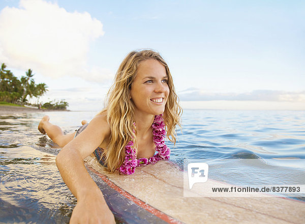 A Young Woman Wearing A Lei Rides A Surfboard Out In The Water Maui  Hawaii  United States Of America