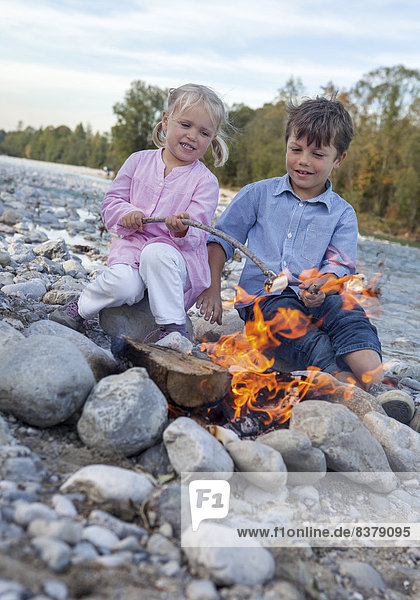 Zwei Kinder sitzen am Lagerfeuer am Fluß