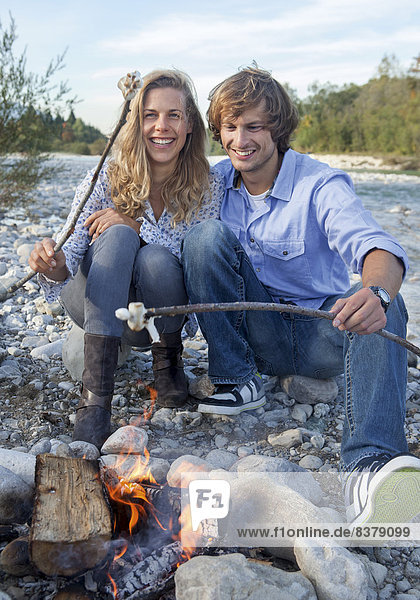 Paar sitzt am Lagerfeuer am Fluß