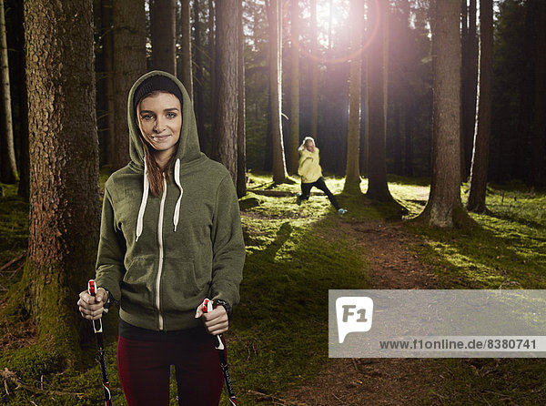 Frau mit Nordic-Walking-Stöcken im Wald  hinten läuft eine weitere Frau  Tirol  Austria