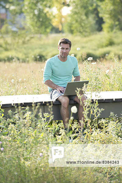 Man using laptop computer while sitting out in countryside