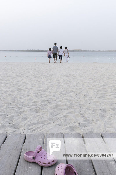 Clogs verlassen auf einem Spazierweg am Strand  Familie nähert sich dem Wasser im Hintergrund