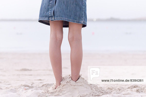 Mädchen am Strand stehend mit im Sand vergrabenen Füßen  niedriger Schnitt