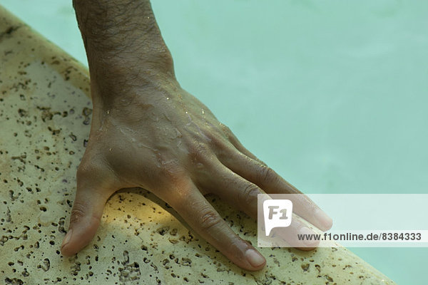 Man's nasse Hand auf der Seite des Pools