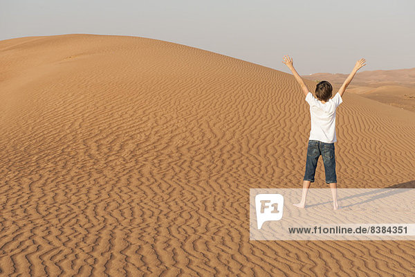Teenager Junge in der Wüste stehend mit erhobenen Armen  Rückansicht