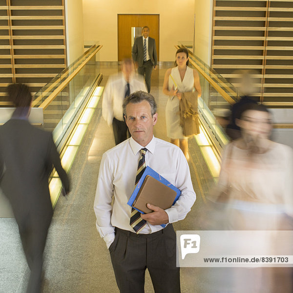 Businessman standing in busy office corridor