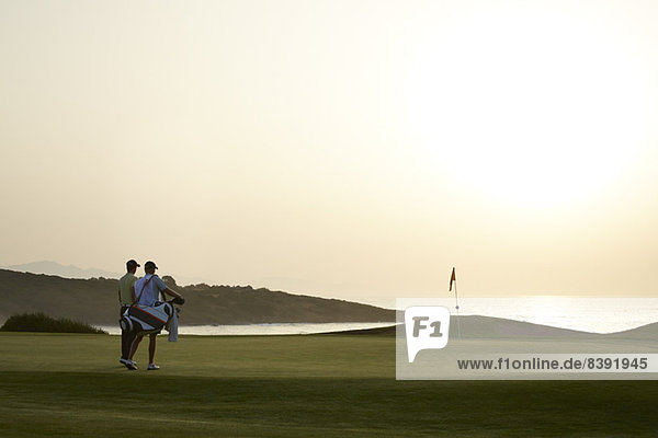 Männer auf dem Golfplatz bei Sonnenuntergang