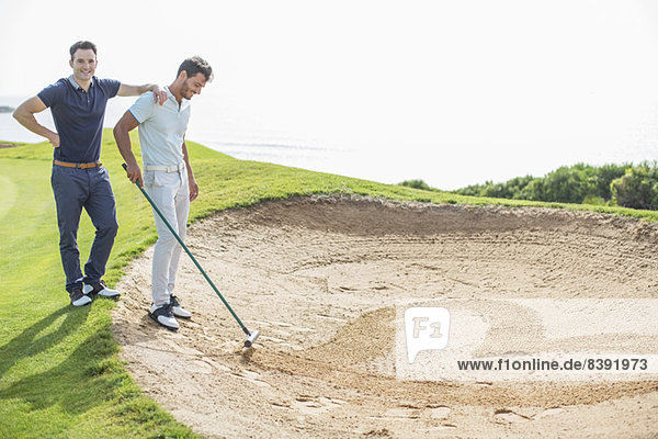 Männer  die in einer Sandfalle auf dem Golfplatz herzförmig rechen.