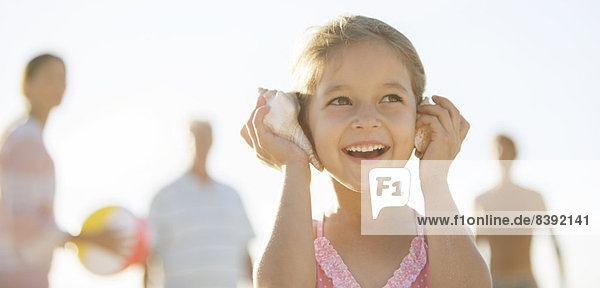 Mädchen hört Muschelschalen am Strand