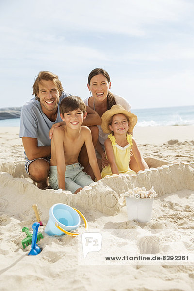 Familie sitzt in einer Sandburg am Strand
