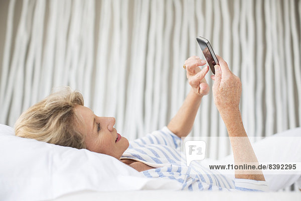 Ältere Frau mit Handy im Bett