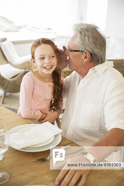 Älterer Mann und Enkelin flüstern bei Tisch