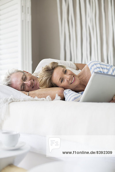 Älteres Paar mit digitalem Tablett auf dem Bett