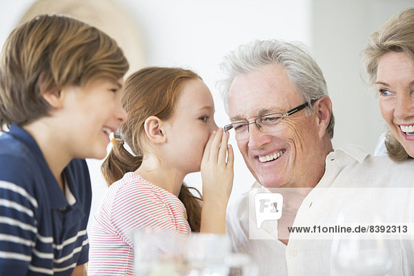Girl whispering to grandfather at table