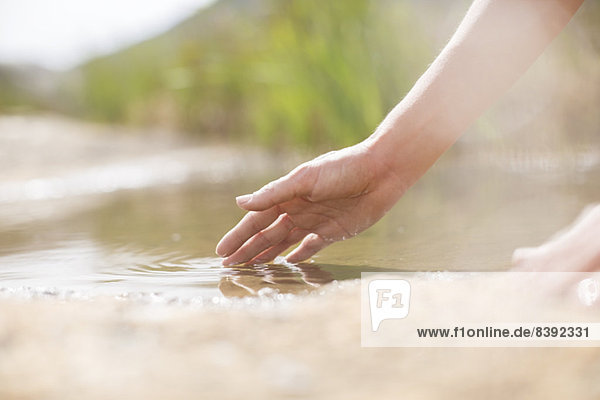 Woman dipping fingers in rural pond