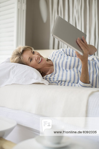 Ältere Frau mit digitalem Tablett auf dem Bett