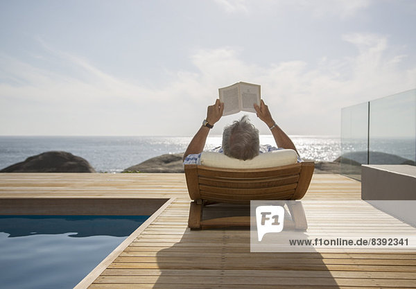 Älterer Mann beim Lesen am Pool