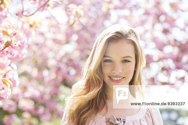 Frau lächelt unter Baum mit rosa Blüten