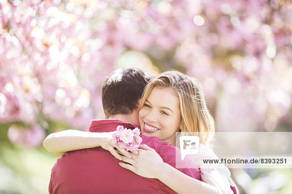 Paar umarmend unter Baum mit rosa Blüten