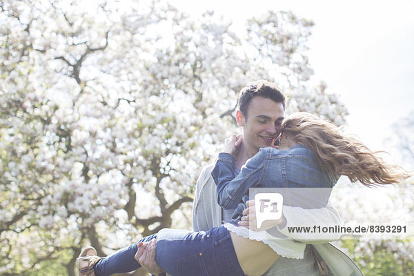 Mann hebt Frau unter Baum mit weißen Blüten