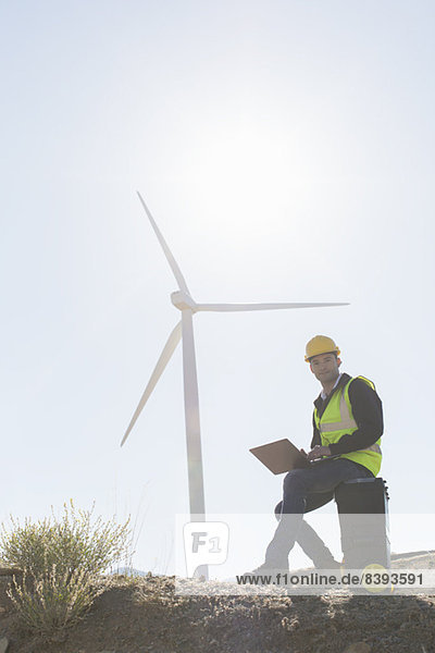 Arbeiter mit Laptop per Windkraftanlage in ländlicher Landschaft