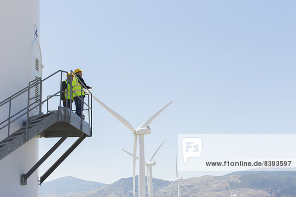 Arbeiter,  die auf einer Windkraftanlage in ländlicher Landschaft stehen
