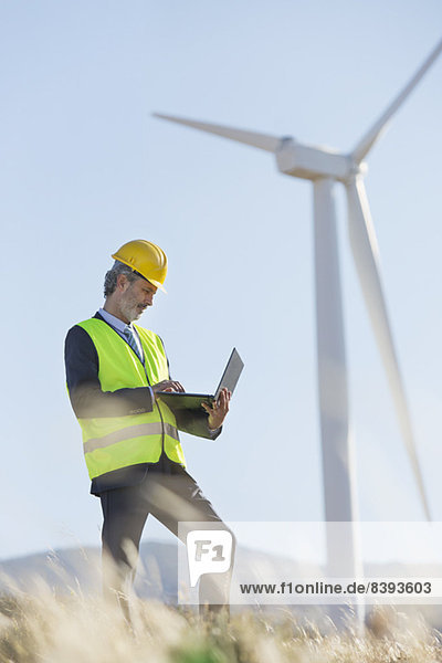 Arbeiter mit Laptop per Windkraftanlage in ländlicher Landschaft