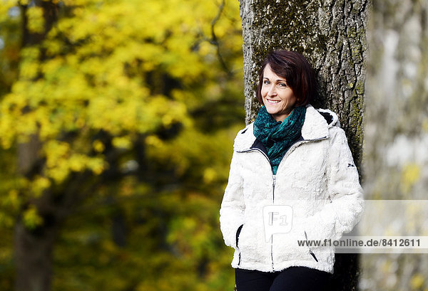 Lächelnde Frau steht an einem Baum im Herbst