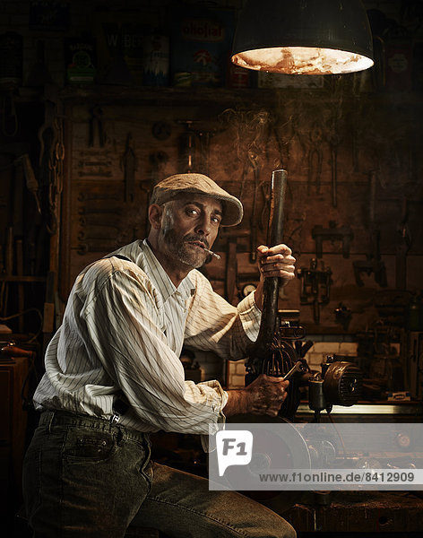 Mann mit Kappe und Zigarette repariert einen Motor in einer Werkstatt