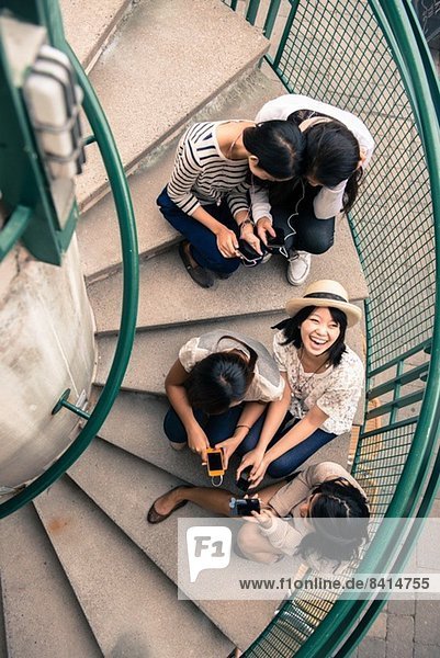 Fünf junge Frauen sitzen auf Stufen und schauen auf Smartphones