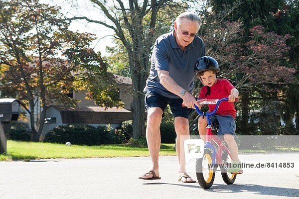 Grandfather encouraging young boy to ride bicycle