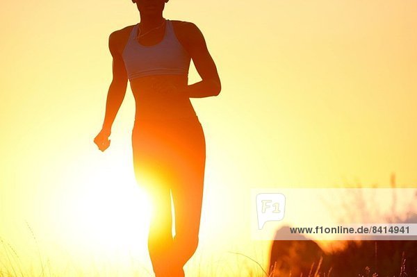 Silhouette einer jungen Frau  die bei Sonnenuntergang läuft.