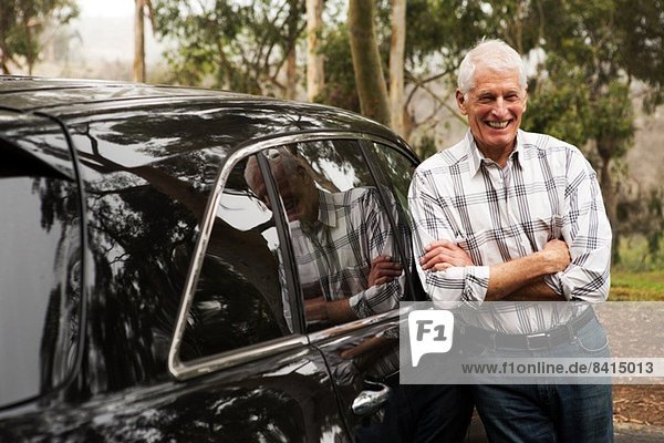 Älterer Mann steht gegen schwarzes Fahrzeug