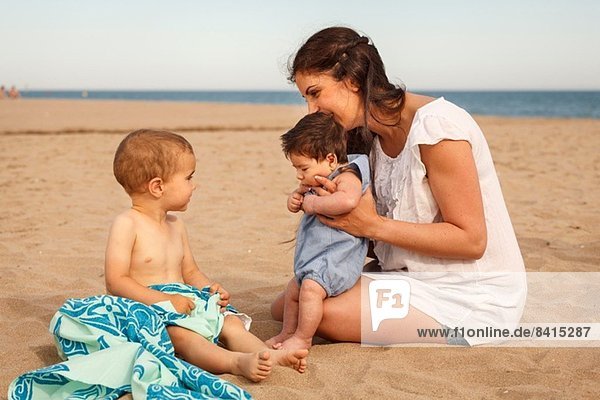 Mutter und Babys am Strand sitzend