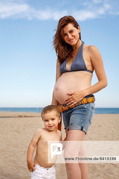 Schwangere Frau am Strand  Hand auf dem Bauch  mit Kleinkind