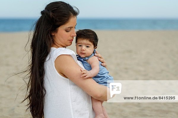 Mutter am Strand trägt Baby in den Armen