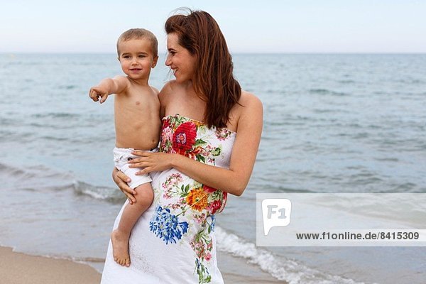 Pregnant woman holding toddler on beach