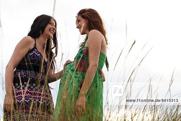 Schwangere Frau und Freundin  im hohen Gras stehend