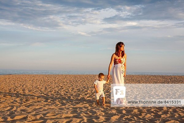 Mother and toddler walking along beach  holding hands