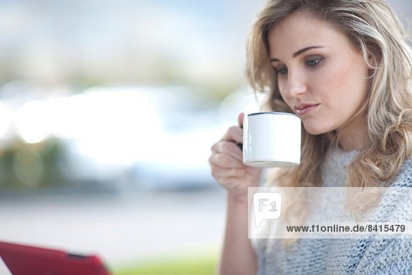 Junge Frau sitzt vor dem Café mit Tasse Kaffee und digitalem Tablett