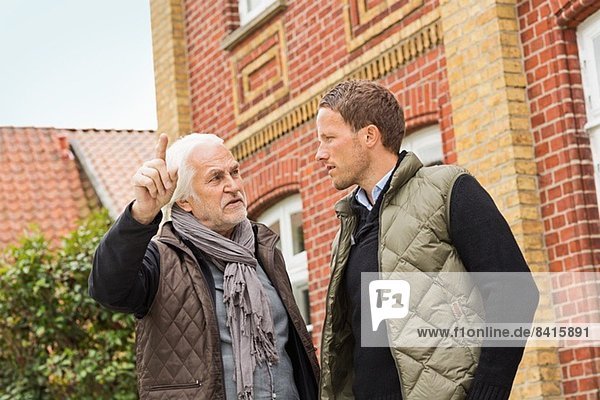 Vater und Sohn vor dem Gebäude  älterer Mann zeigt auf