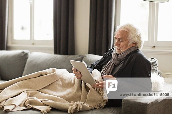 Senior man using digital tablet with blanket