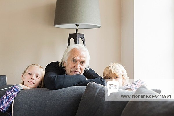 Portrait of grandfather and grandchildren leaning on sofa