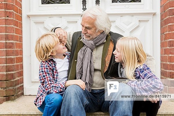 Großvater sitzend mit Enkeln vor der Haustür