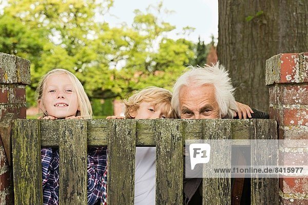 Großvater und Enkelkinder blicken über Holztor