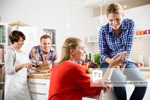 Zwei Frauen mit Handy in der Küche  Mutter und Bruder im Hintergrund