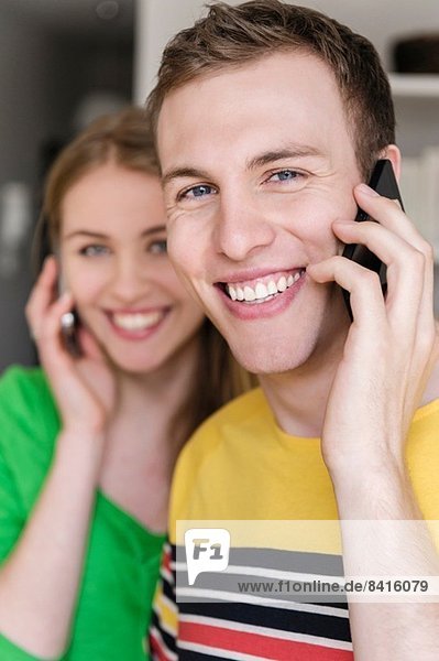 Junger Mann am Handy mit Frau im Hintergrund