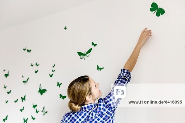 Junge Frau dekoriert Wand mit grünen Schmetterlingen